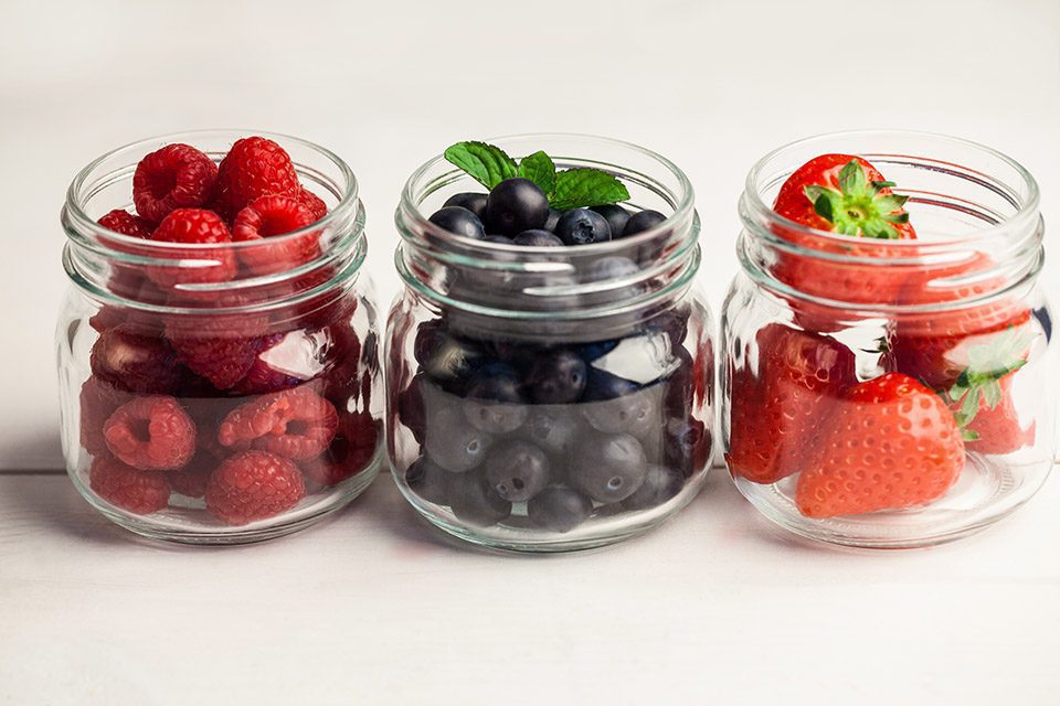 Glass jars of fresh berries on wooden table